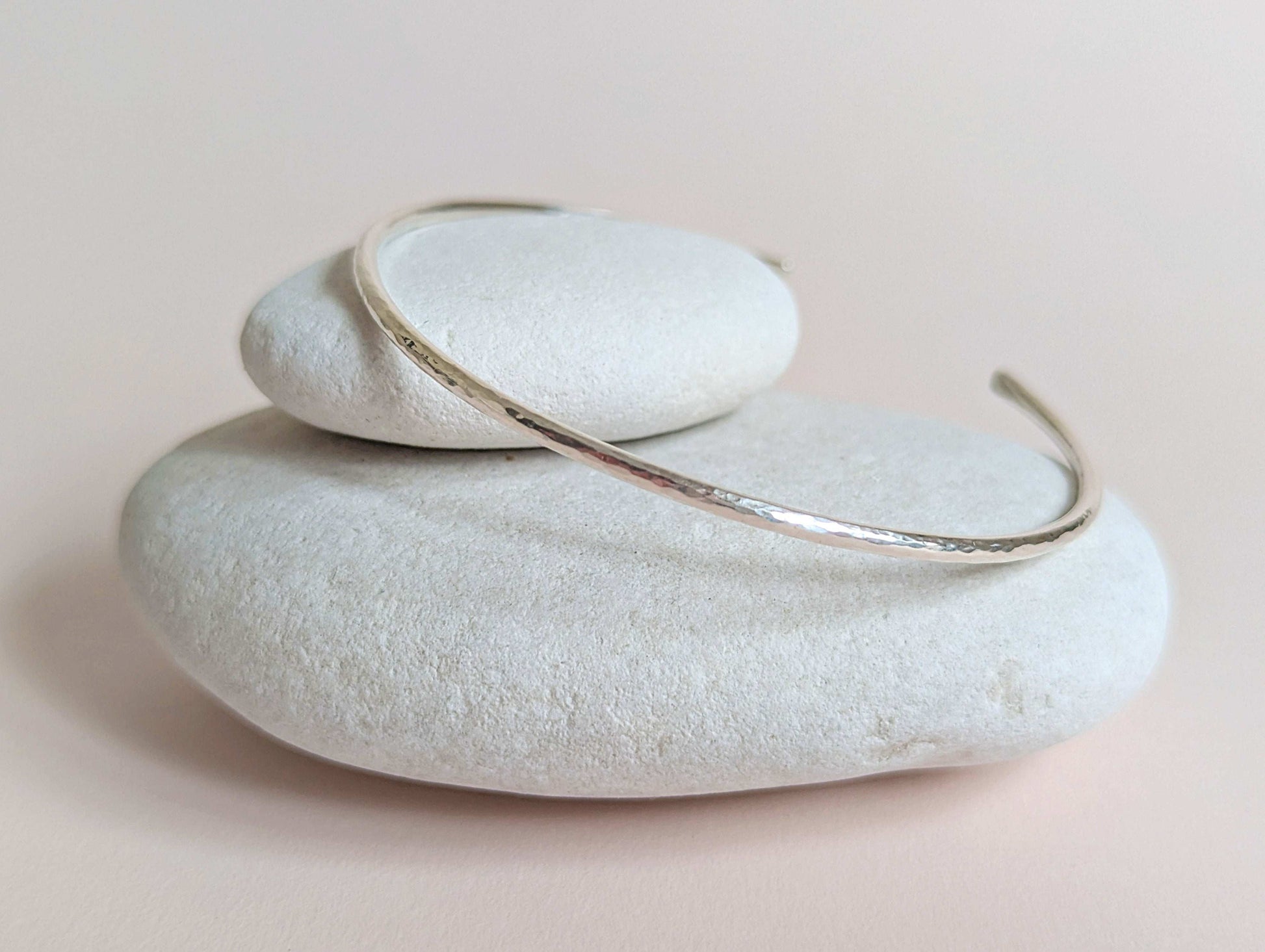 Silver bracelet on a stack of white stones with a soft pink background