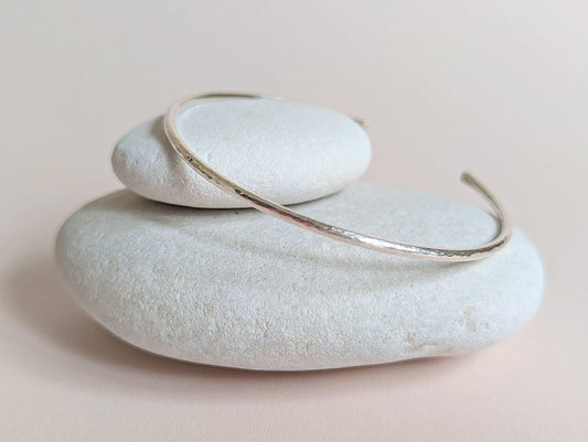 Silver bracelet on a stack of white stones with a soft pink background