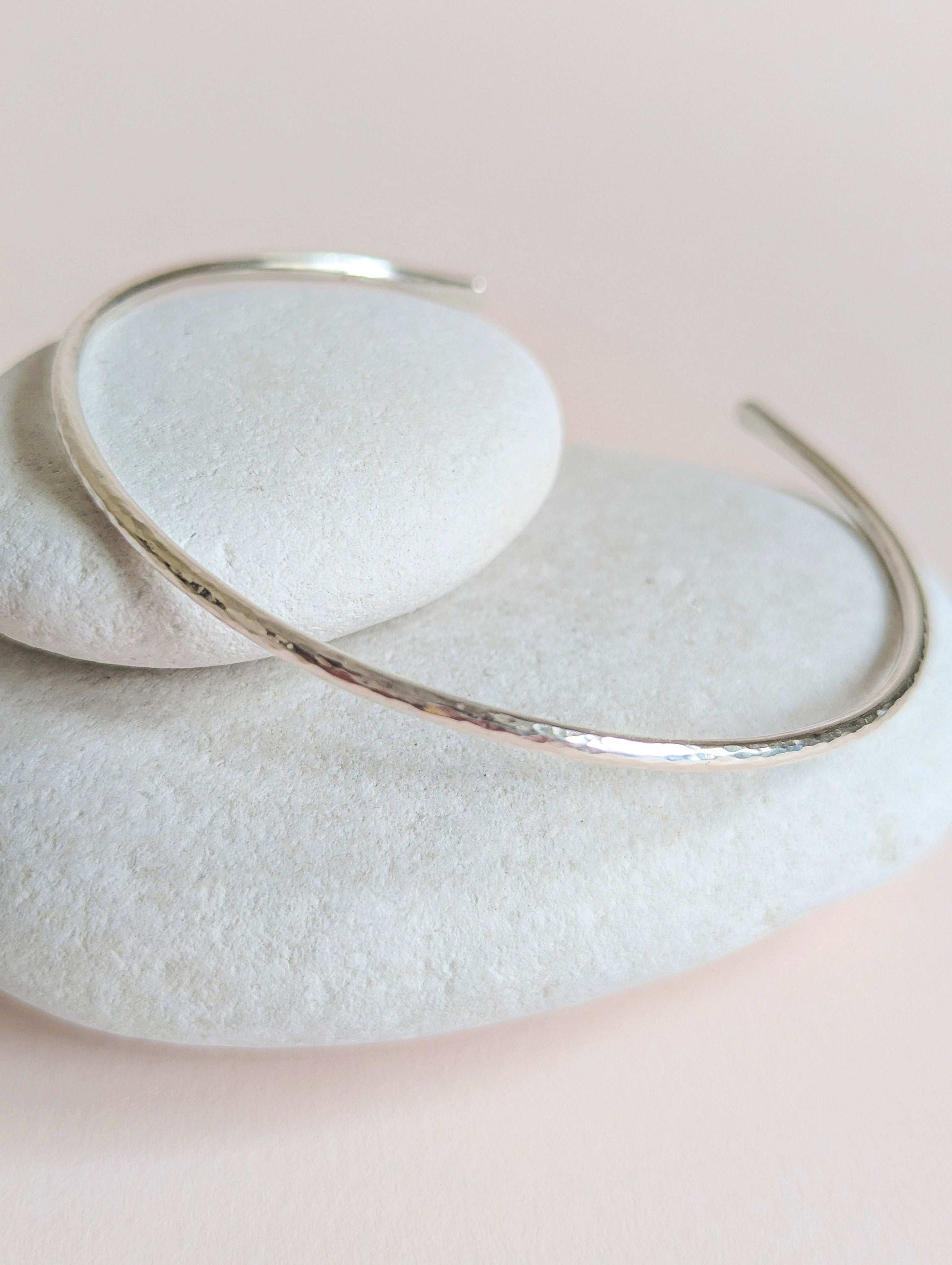 Silver bangle on a light stone surface with a soft pink background