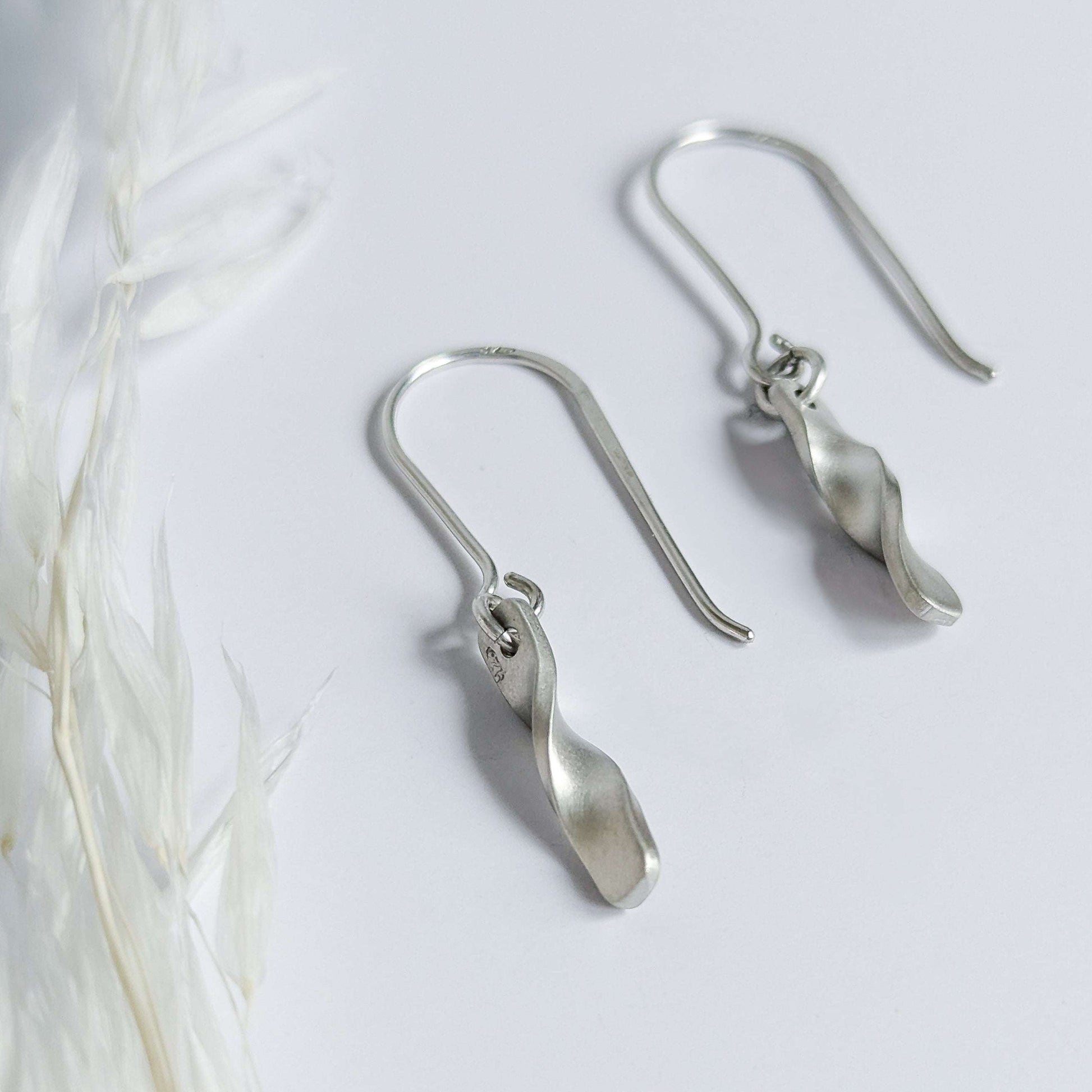 Minimalist satin brushed sterling silver twist drop earrings - side view laid flat