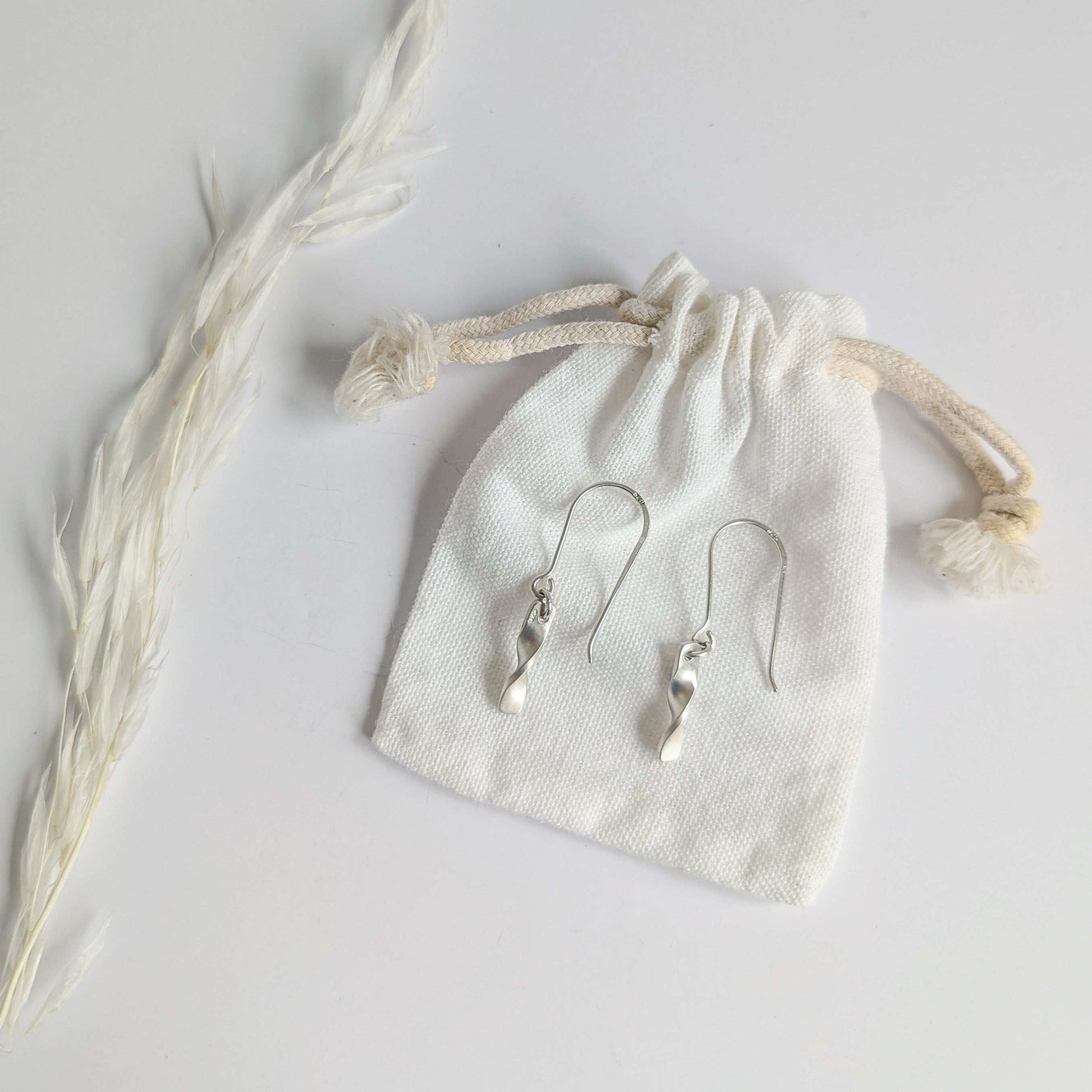 Minimalist satin brushed sterling silver twist drop earrings - show on white cotton cloth drawstring bag