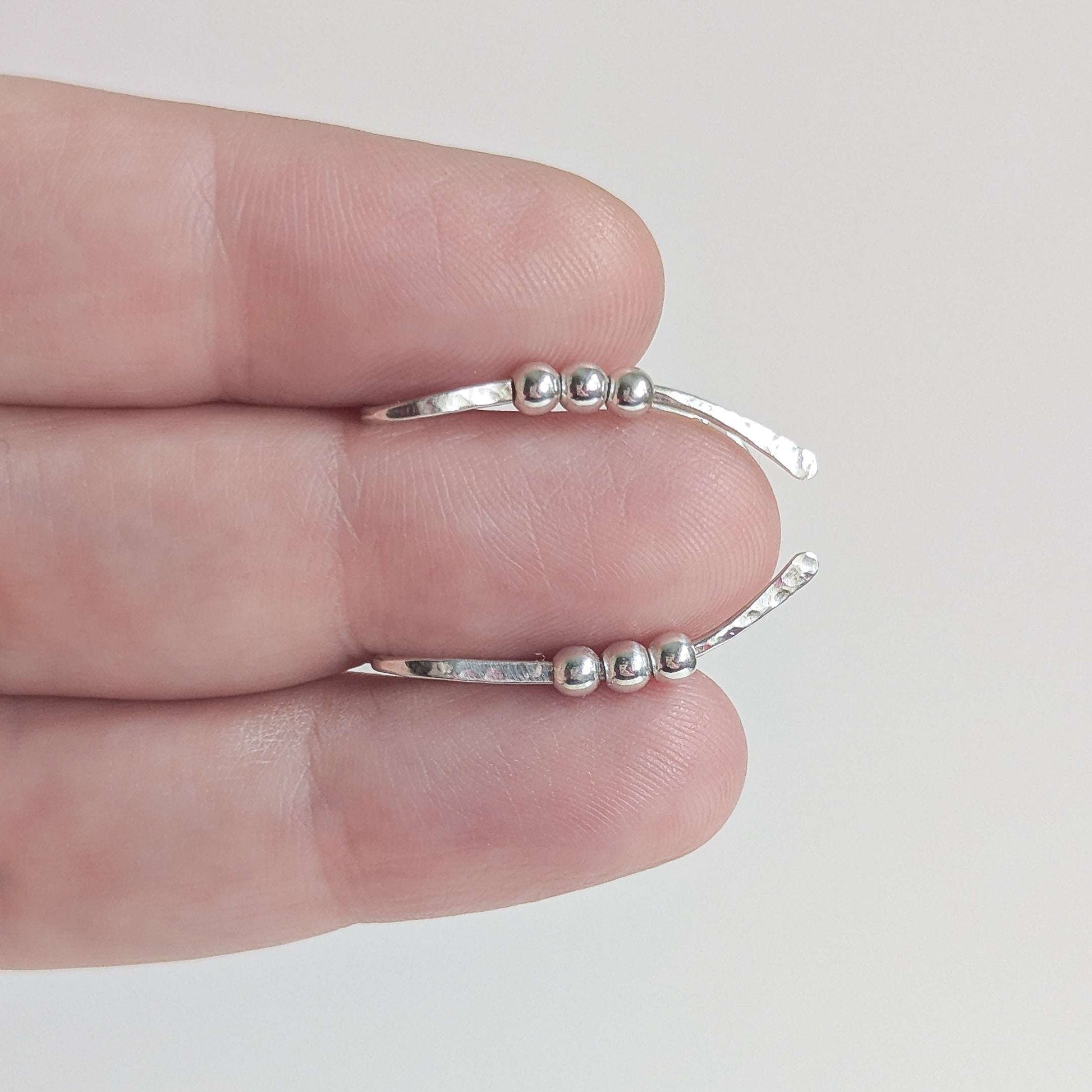 Silver bead ear climber with small beads on a hand against a light gray background