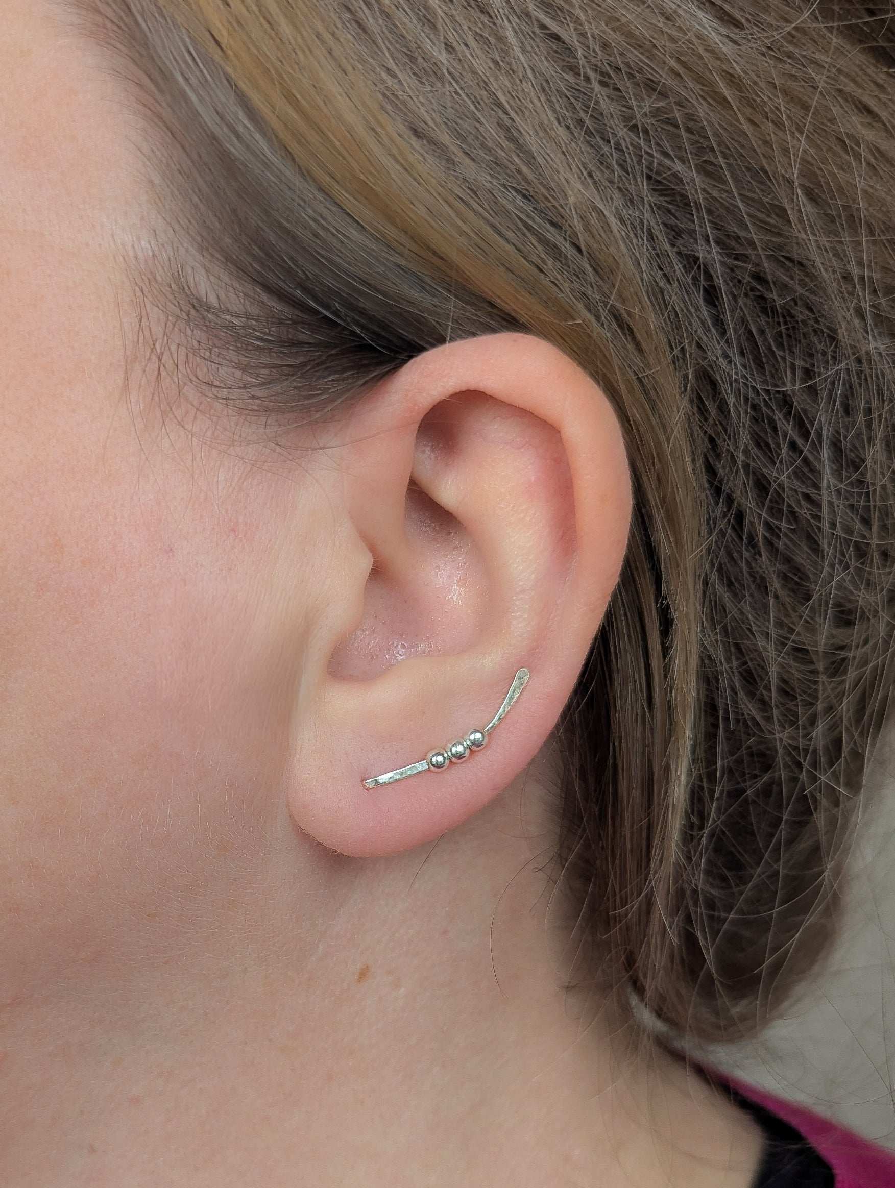 Close-up of an ear wearing a silver  bead ear climber earring with a blurred background