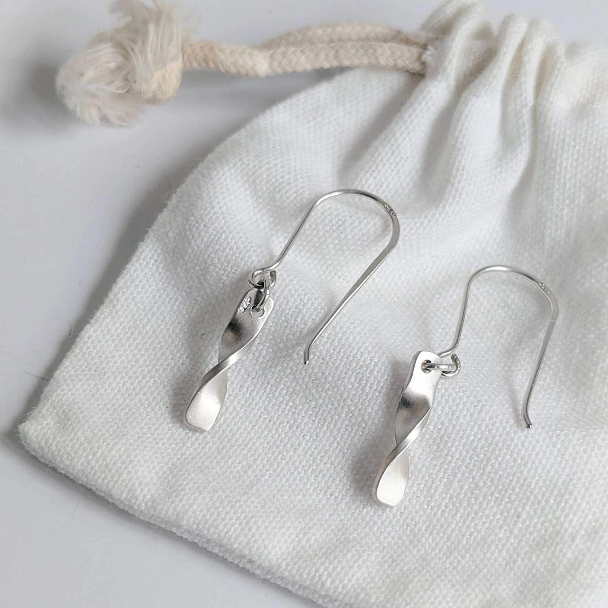 Minimalist satin brushed sterling silver twist drop earrings - shown on white cotton cloth gift bag