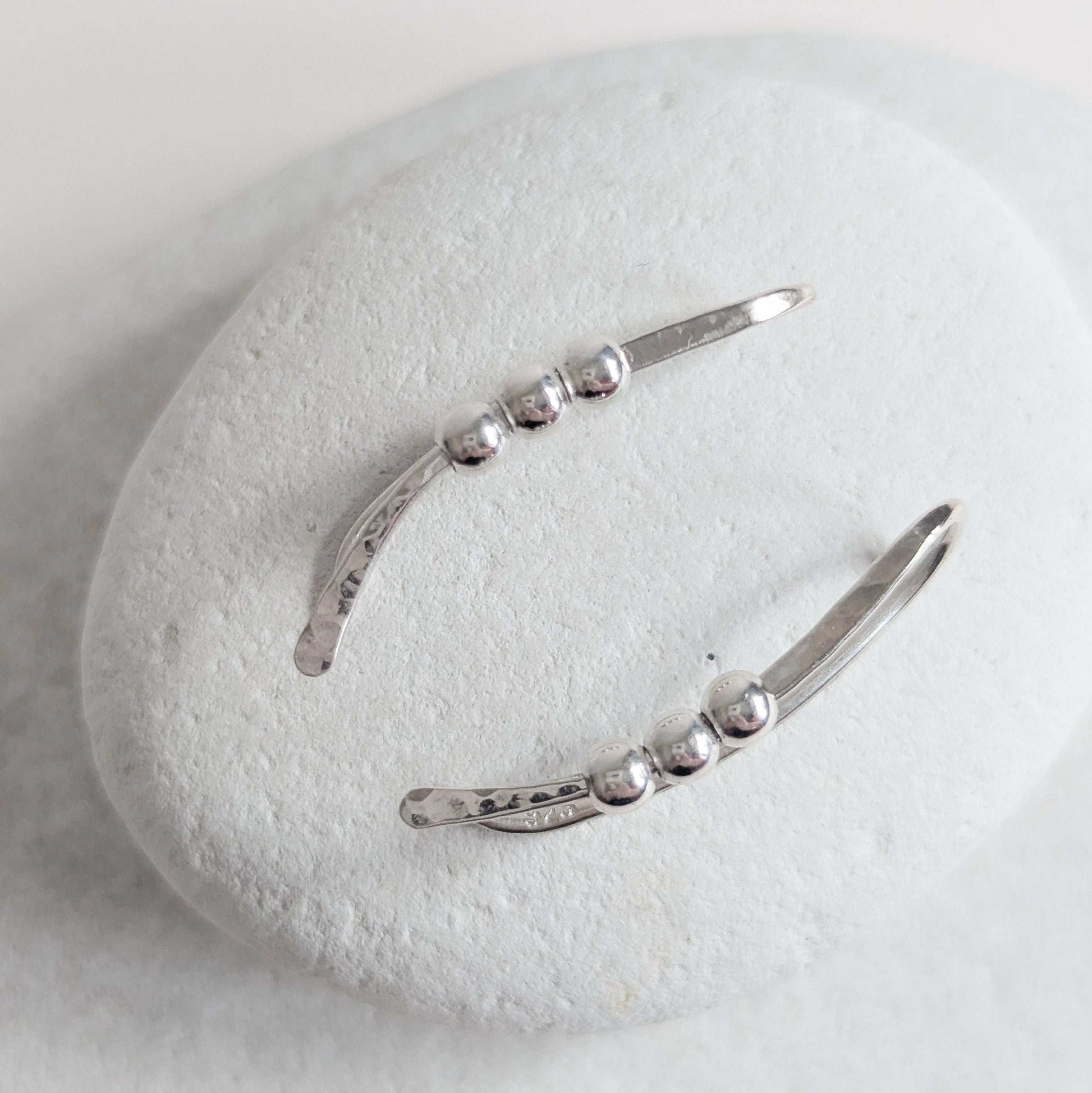 Silver bead ear climber earrings on a white stone surface
