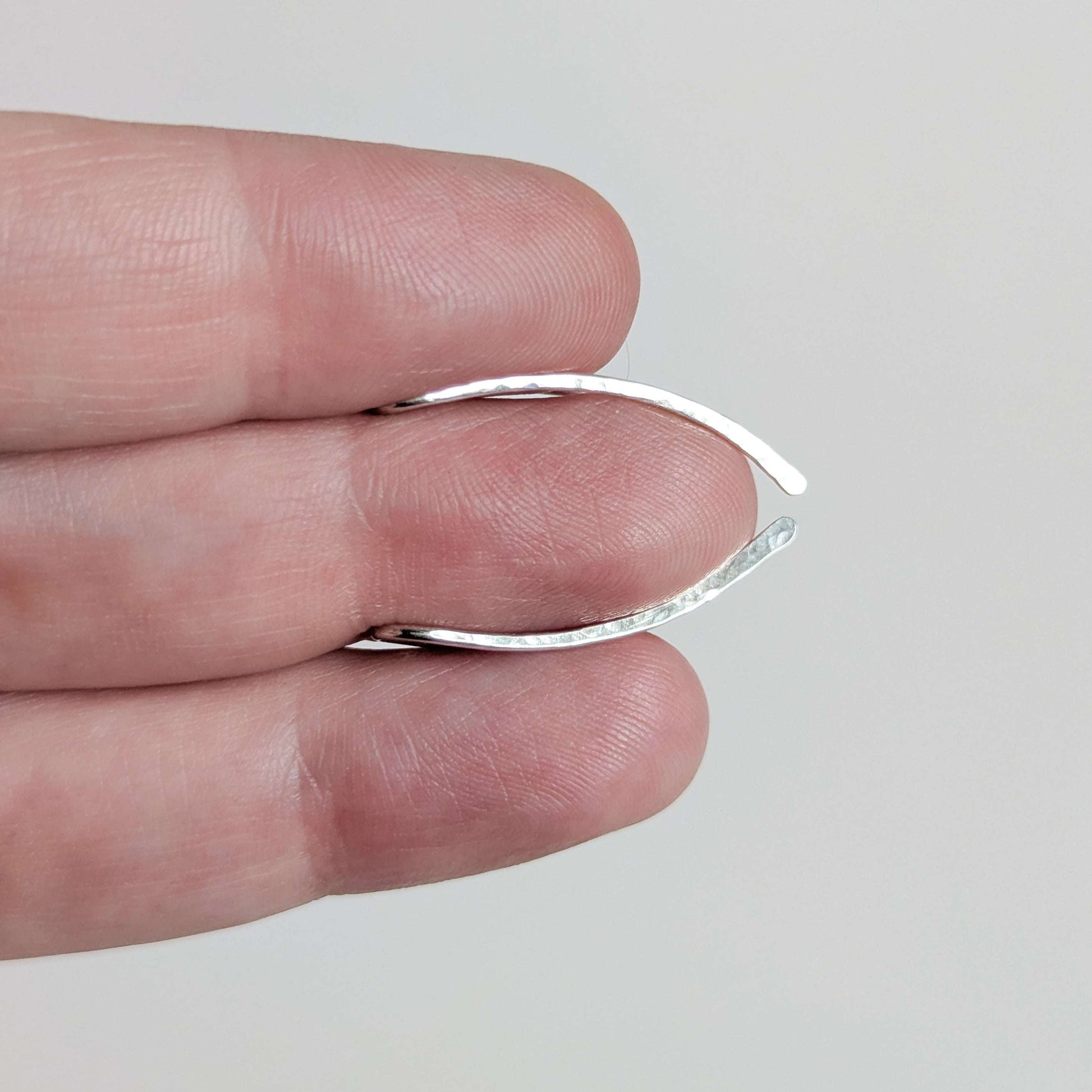 Silver ear climbers being held between two fingers on a plain background