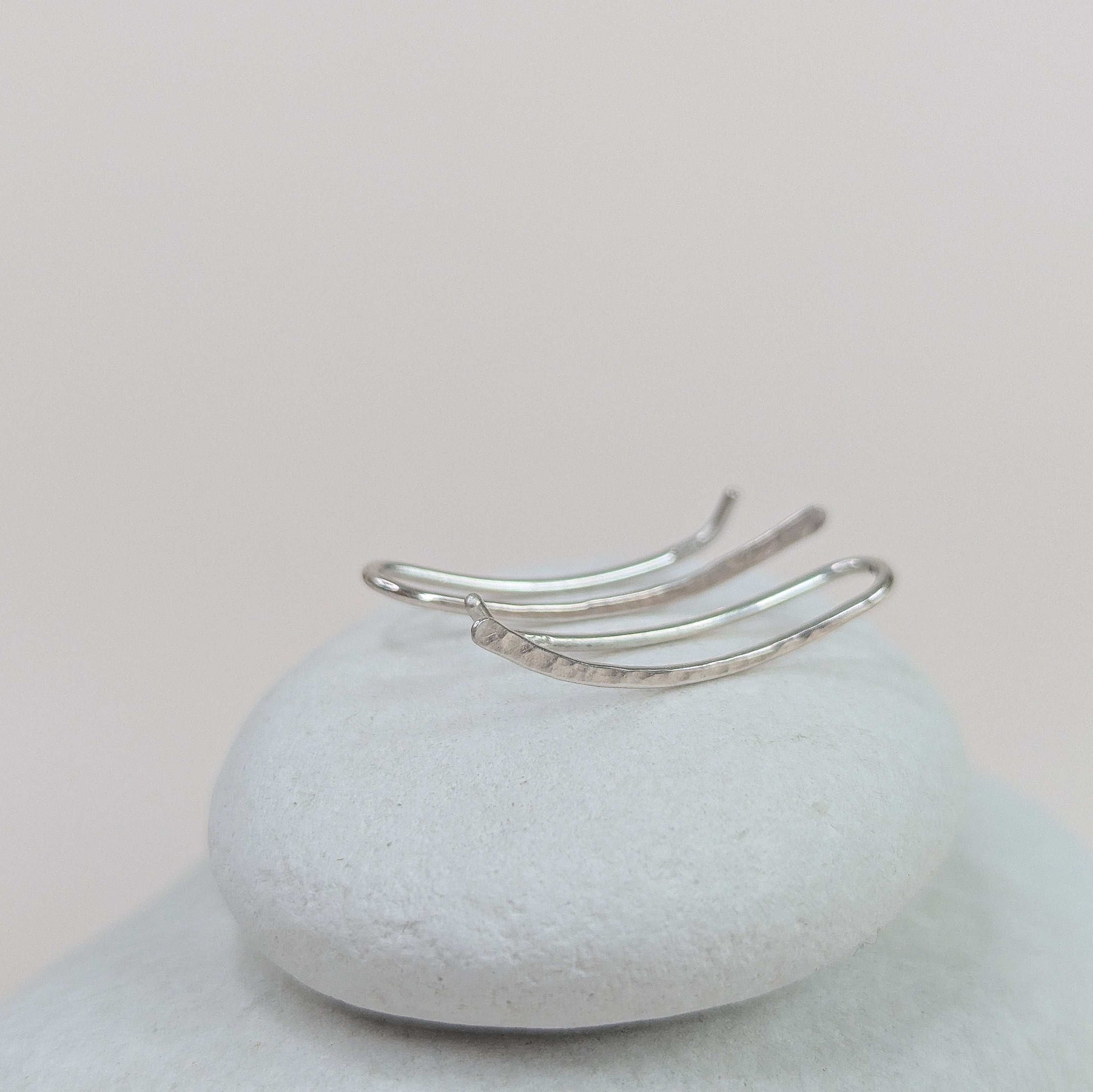 Silver ear climbers on a textured white surface with a light pink background