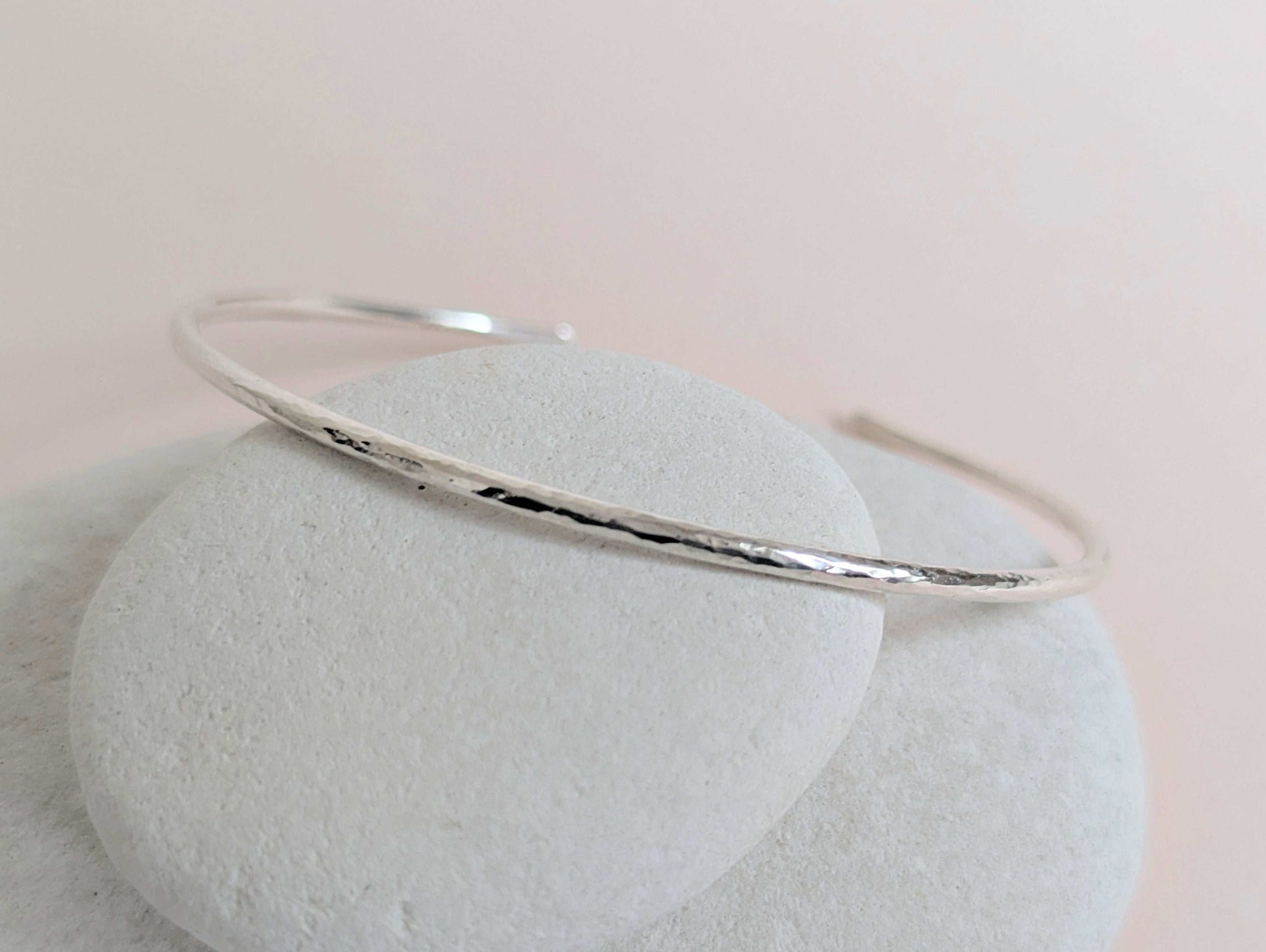 Silver bangle on a light stone surface with a soft pink background