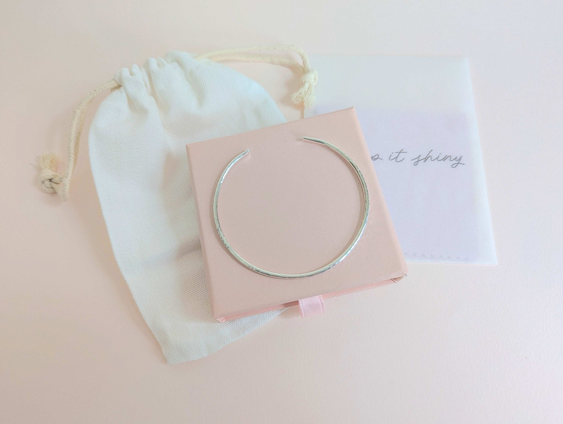 Silver bracelet on a pink jewellery gift box with a white drawstring bag in the background and polishing cloths