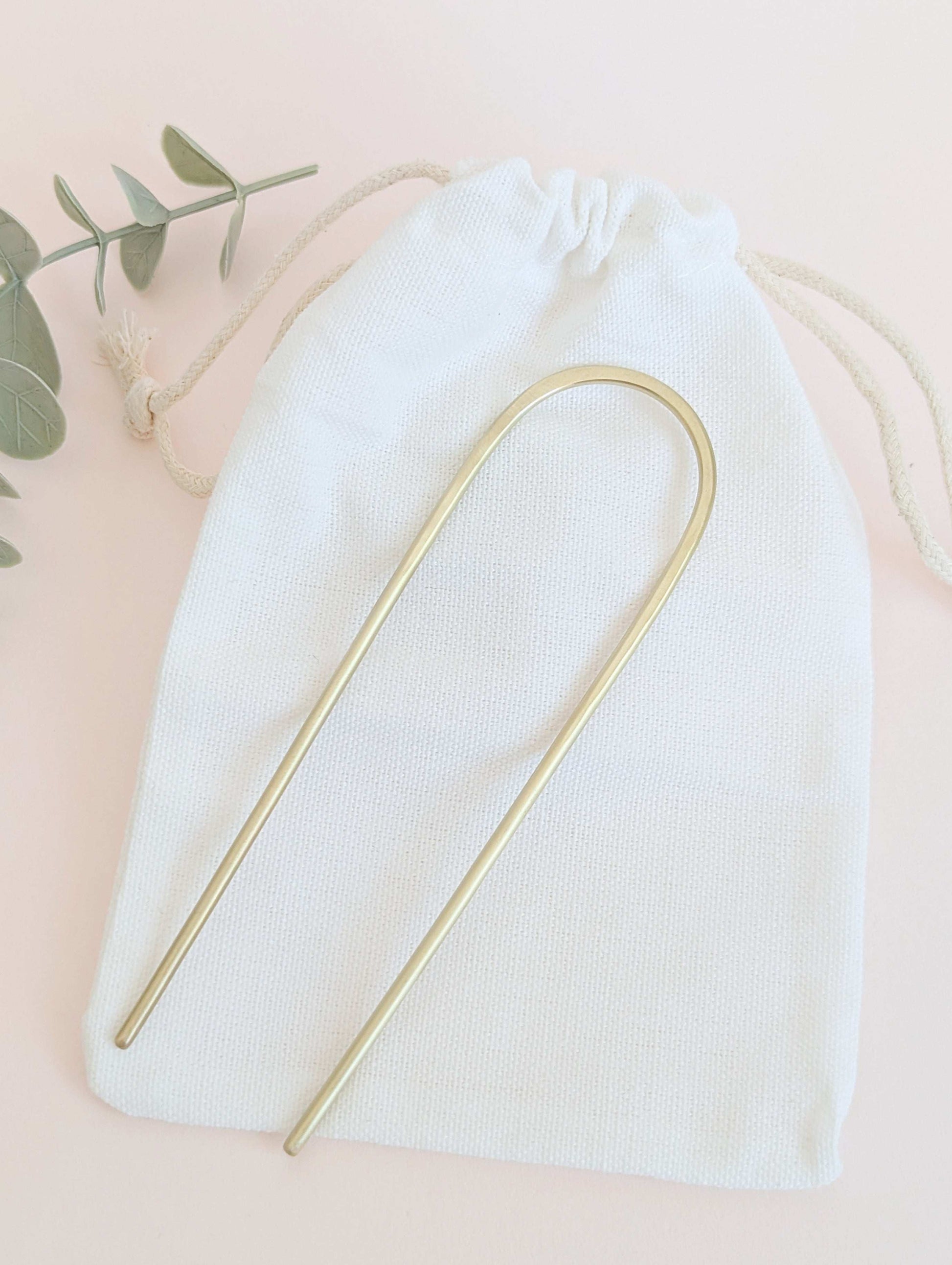 Brushed brass gold round pin hair fork - laid flat on a white drawstring cotton bag
