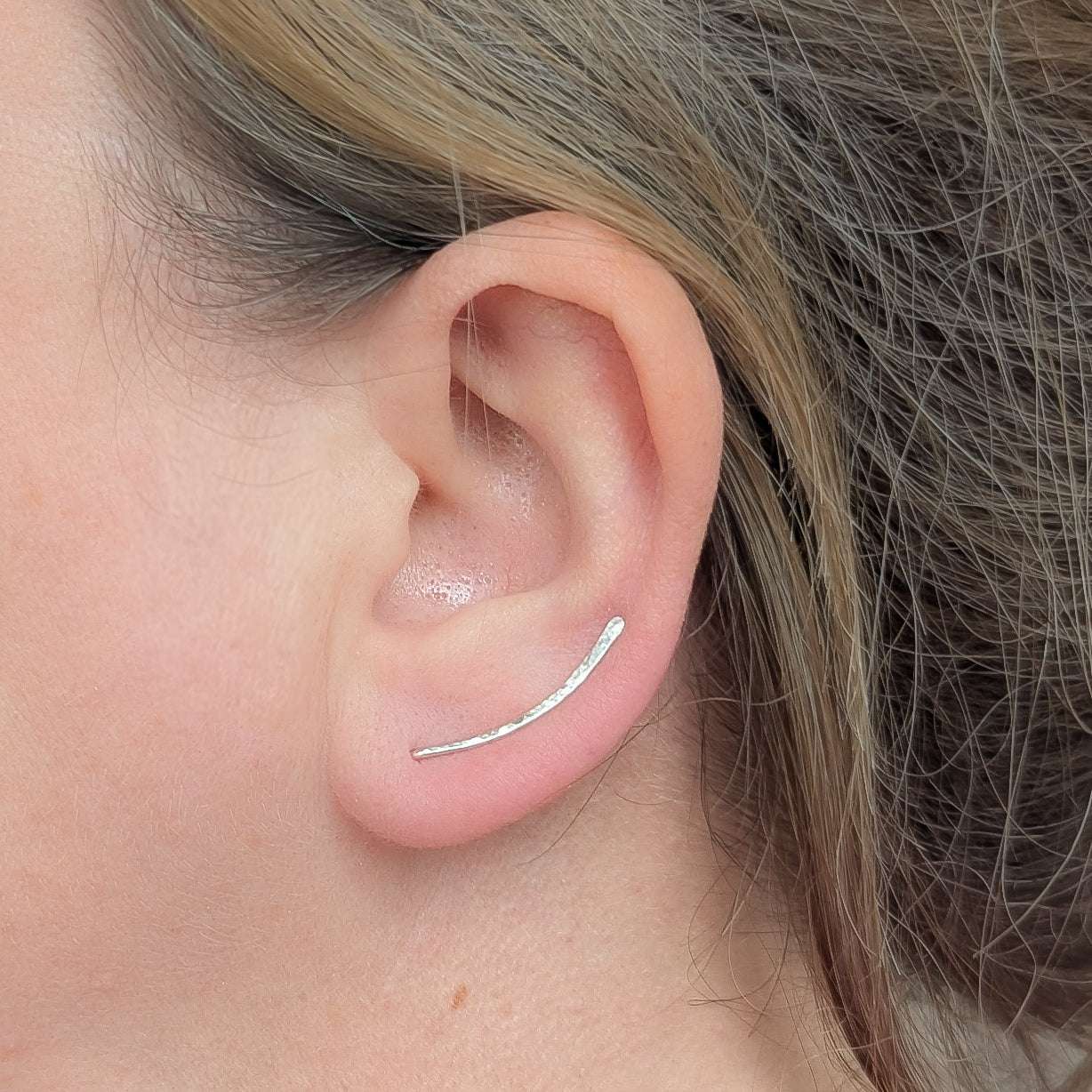 Close-up of an ear wearing a silver ear climber with hair partially covering the frame.