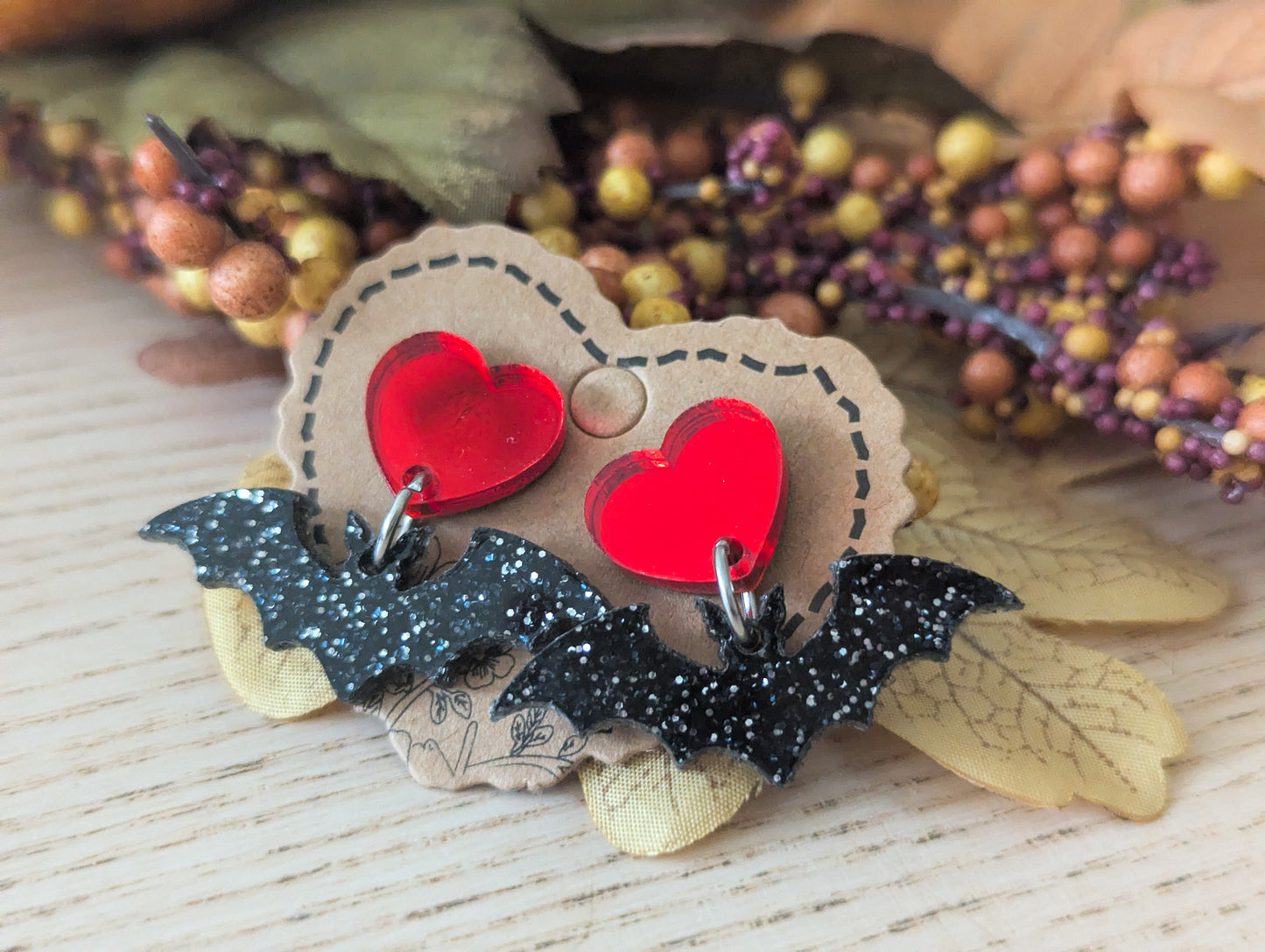 Pair of earrings with red heart and bat design on a wooden surface with decorative elements.