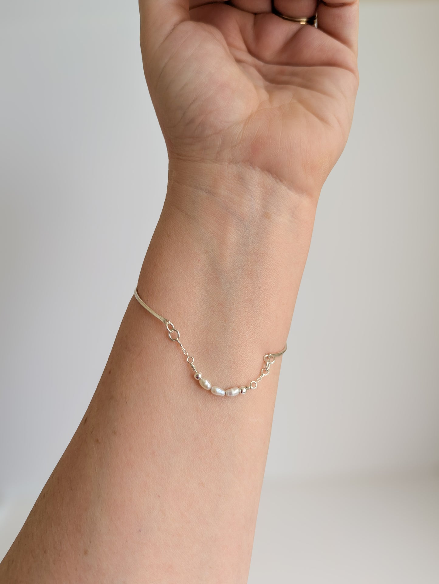 Thin sterling silver dainty cuff bangle with seed pearl bar chain - shows bangle being worn on the wrist, relaxed fit