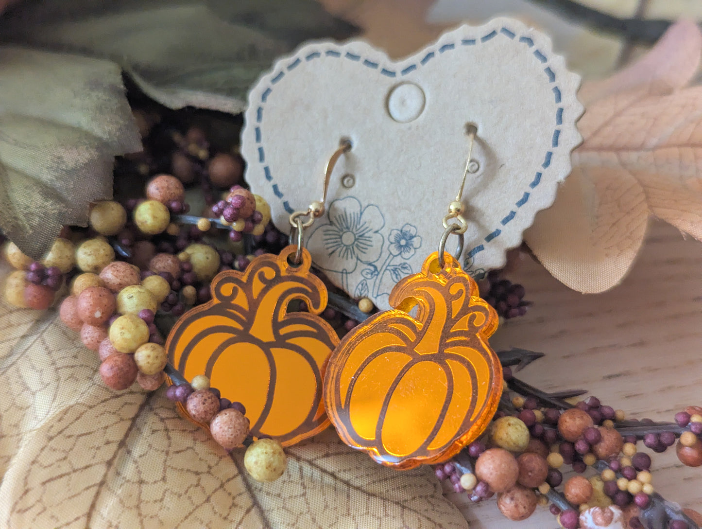 Pumpkin-shaped earrings on a heart-shaped card with berries and leaves.