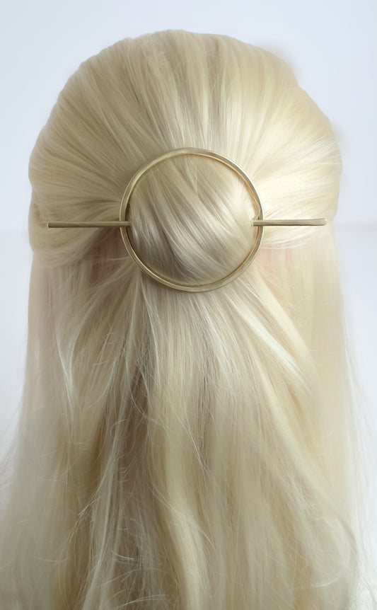 Gold circle brass hairpin in blonde hair against a white background