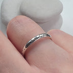 Silver ring with a textured design on a finger against a neutral background