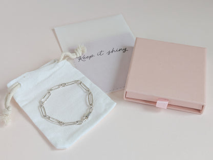 Silver bracelet on a white drawstring bag with 'Keep it shining' text, next to a pink jewelry box on a light pink background.
