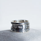 A stack of three silver rings with textured, hammered, and engraved details, resting on a gray stone against a white background.