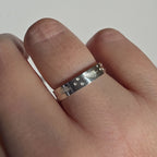 A silver band ring with engraved fern fronds and small raised dots, shown worn on a finger against a plain light background.