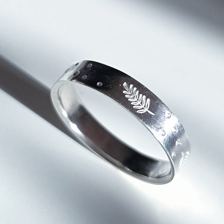 A polished sterling silver band ring featuring a small engraved fern leaf on the outer surface, photographed on a clean white background with a soft shadow.