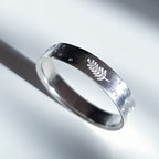 A polished sterling silver band ring featuring a small engraved fern leaf on the outer surface, photographed on a clean white background with a soft shadow.