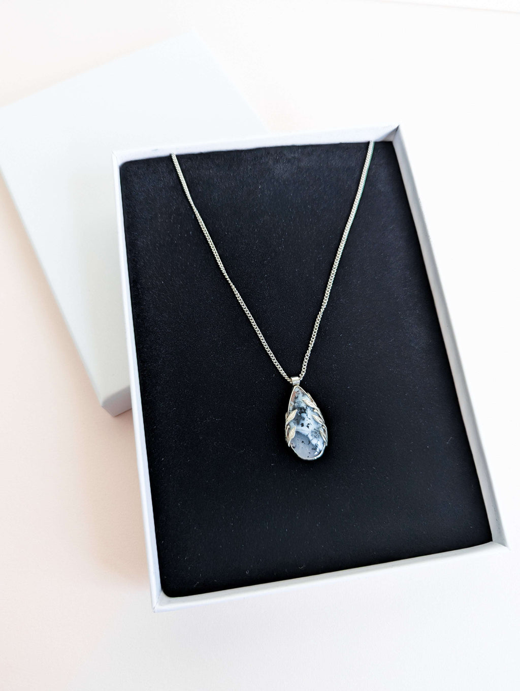 Dendritic snow agate leaf Necklace with a pendant in a white presentation box with black foam insert on a pink background