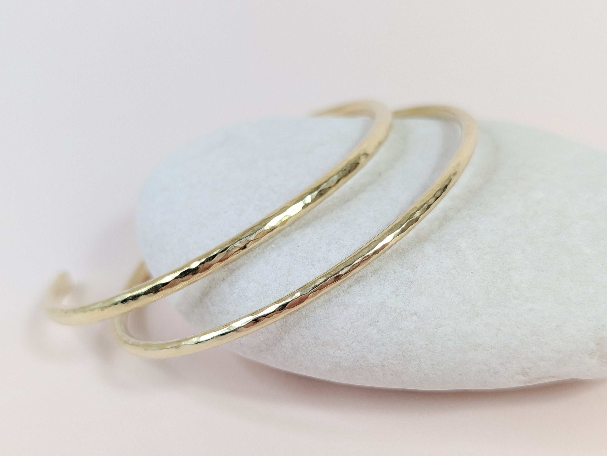 Gold bracelet on a white pebbles with a light pink background