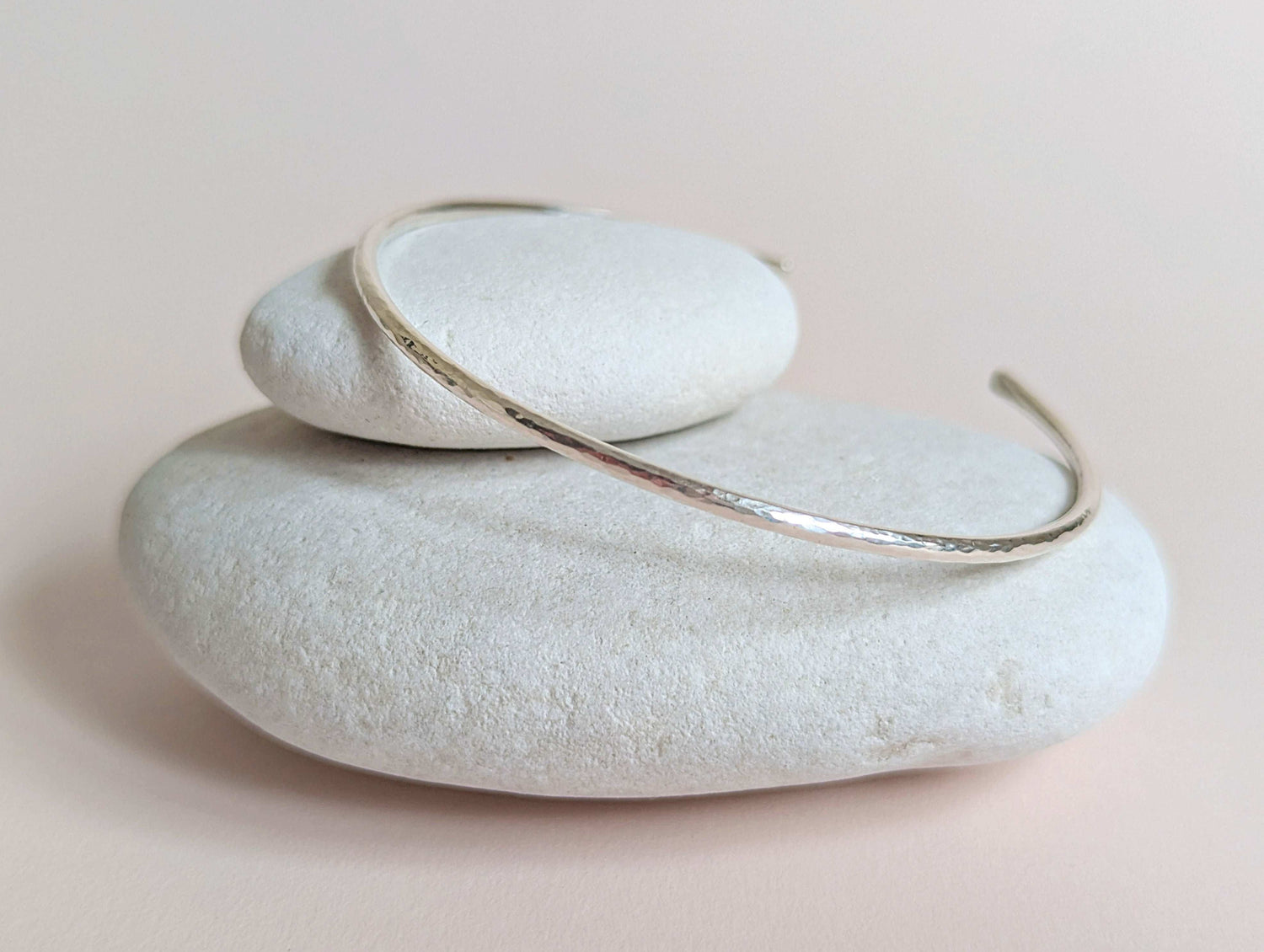 Silver bracelet on a stack of white stones with a soft pink background