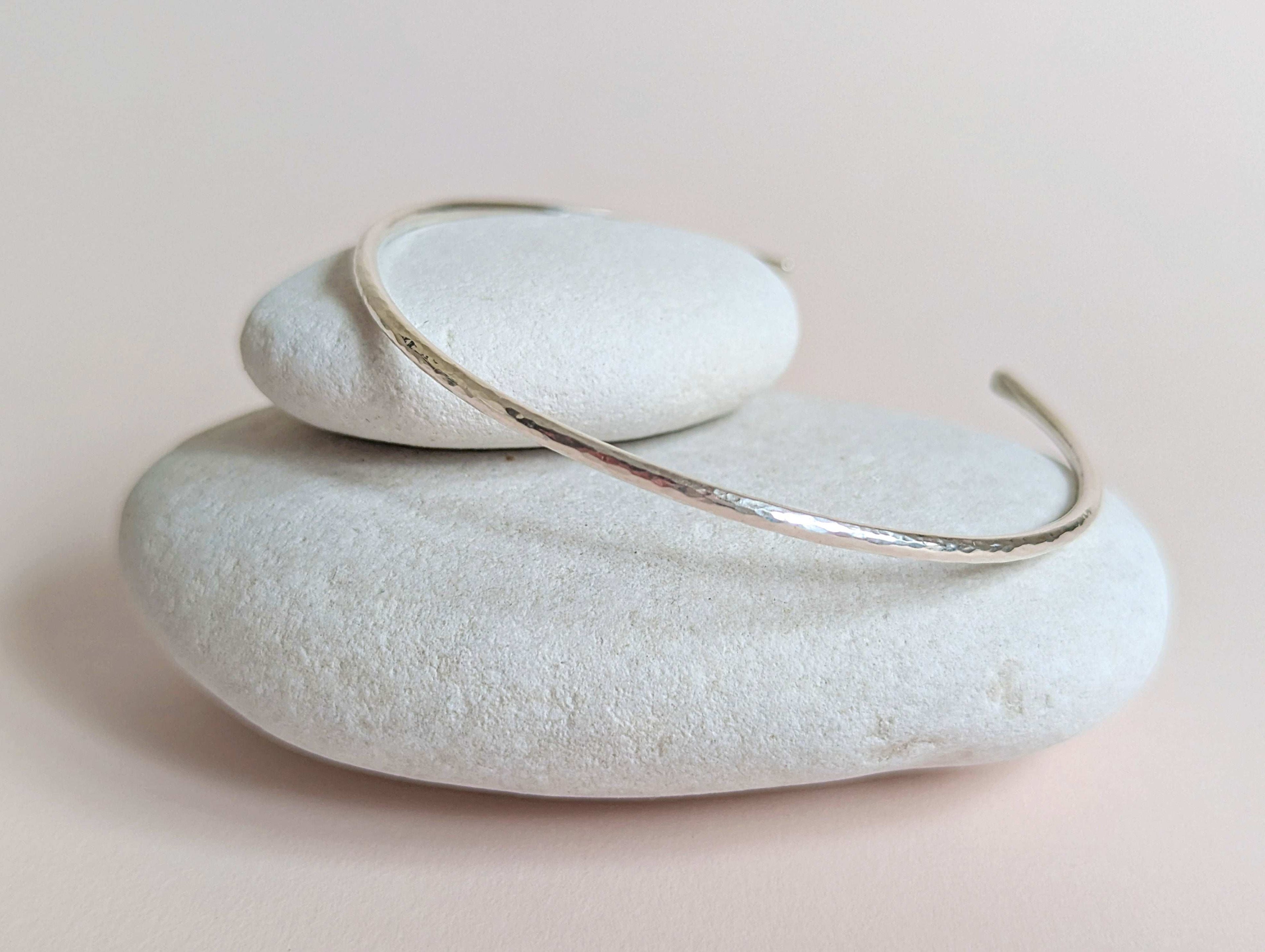Silver bracelet on a stack of white stones with a soft pink background