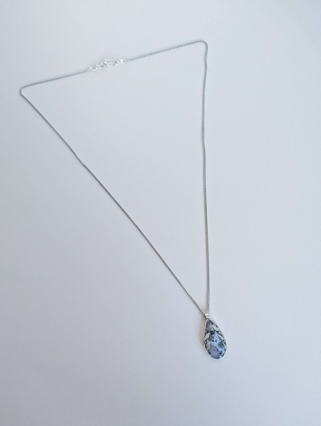 Dendritic snow agate leaf Necklace with a pendant on a light grey surface