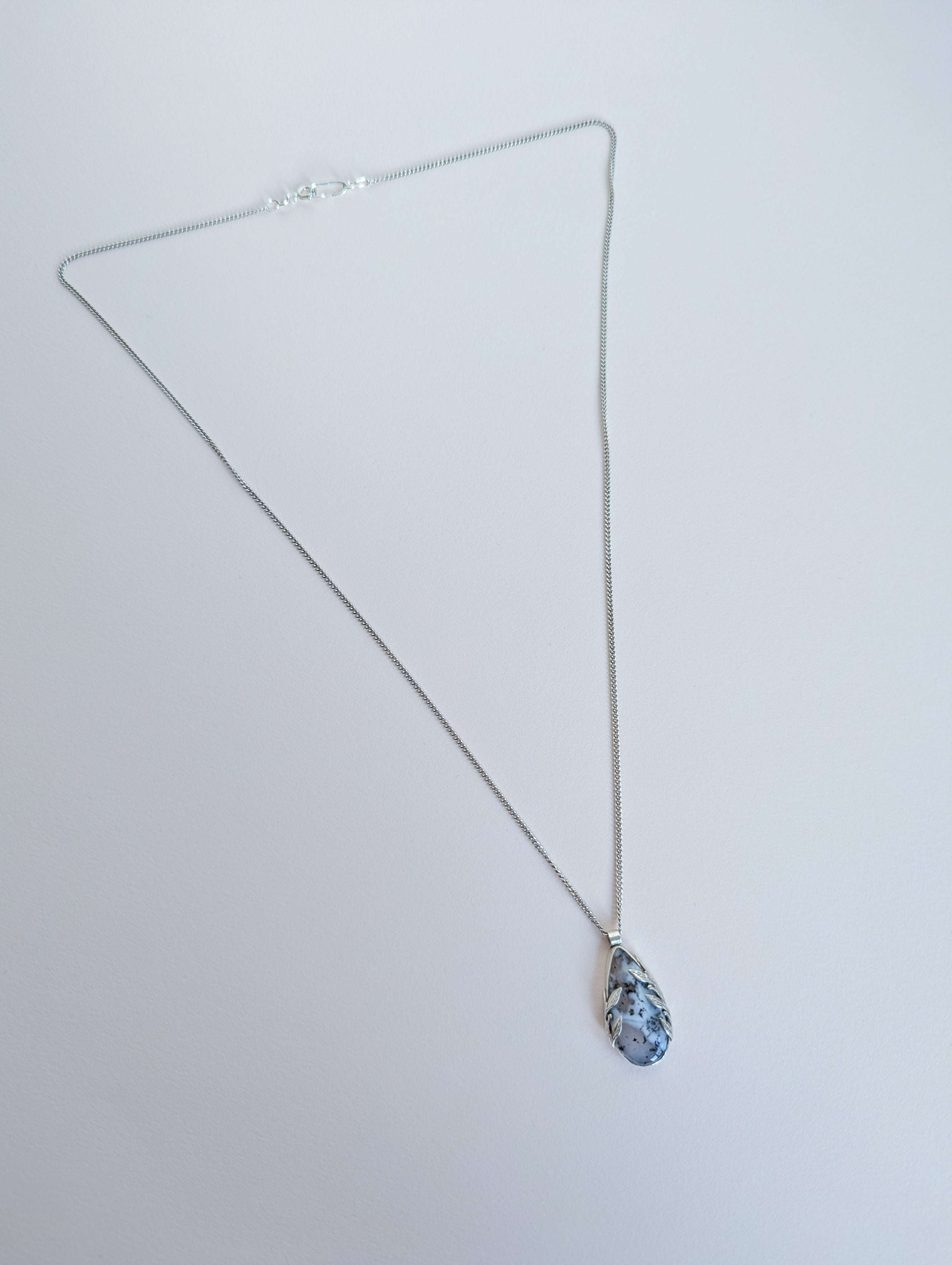 Dendritic snow agate leaf Necklace with a pendant on a light grey surface