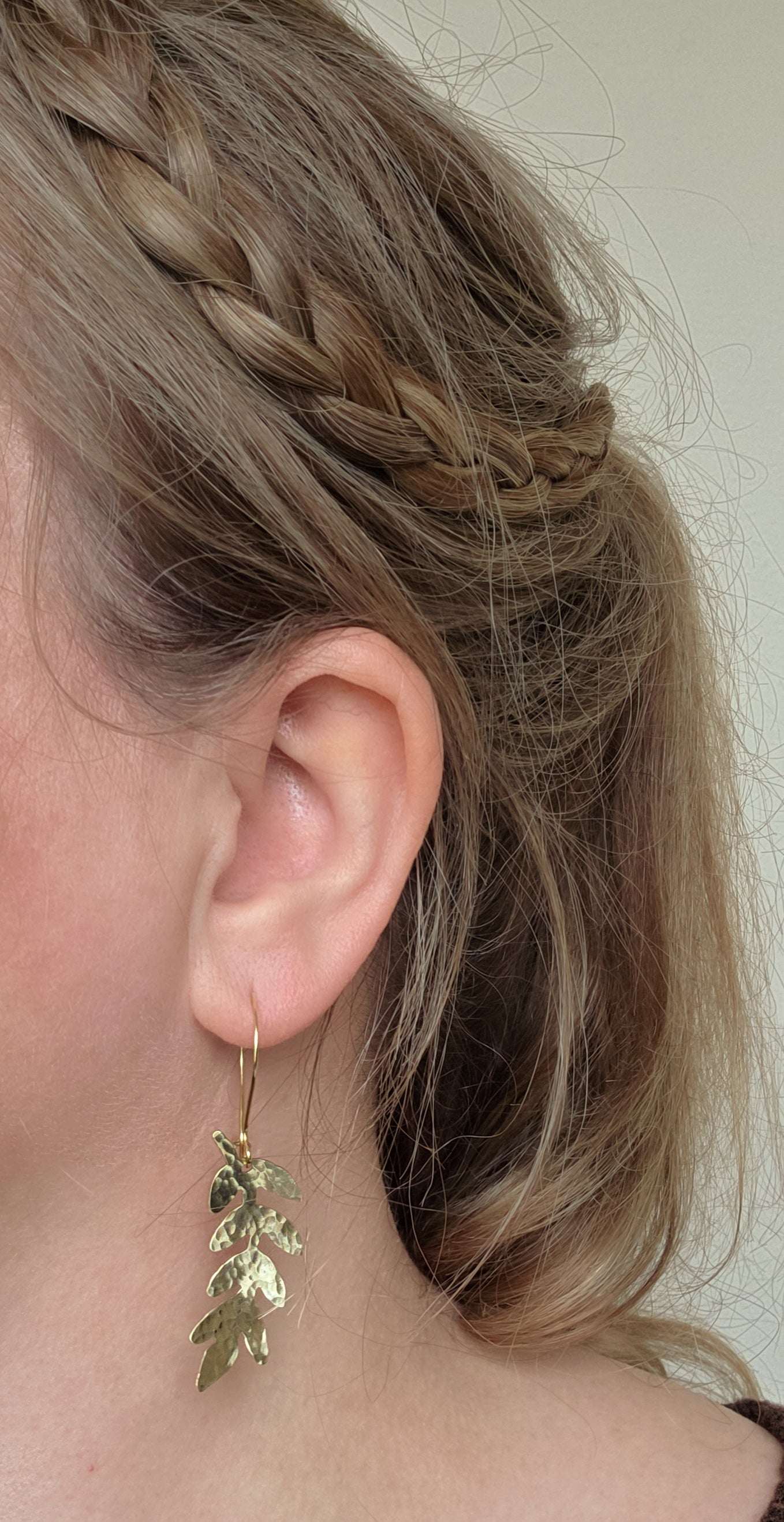 Gold leaf earrings worn by a person with braided hair.