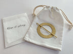 Gold circular brooch in a drawstring bag with a cloth labeled 'Keep it shiny' on a light background