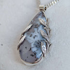 Dendritic snow agate leaf Necklace with a pendant on a light grey surface