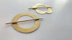 Two gold hair pins with circular designs on a light gray background