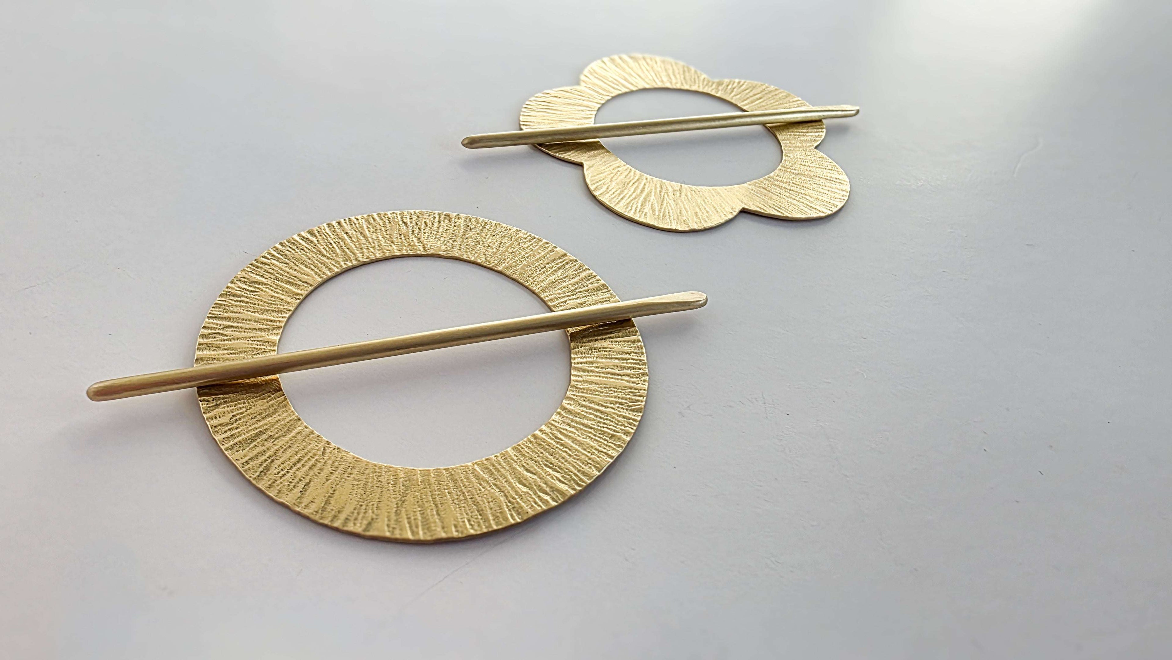 Two gold hair pins with circular designs on a light gray background