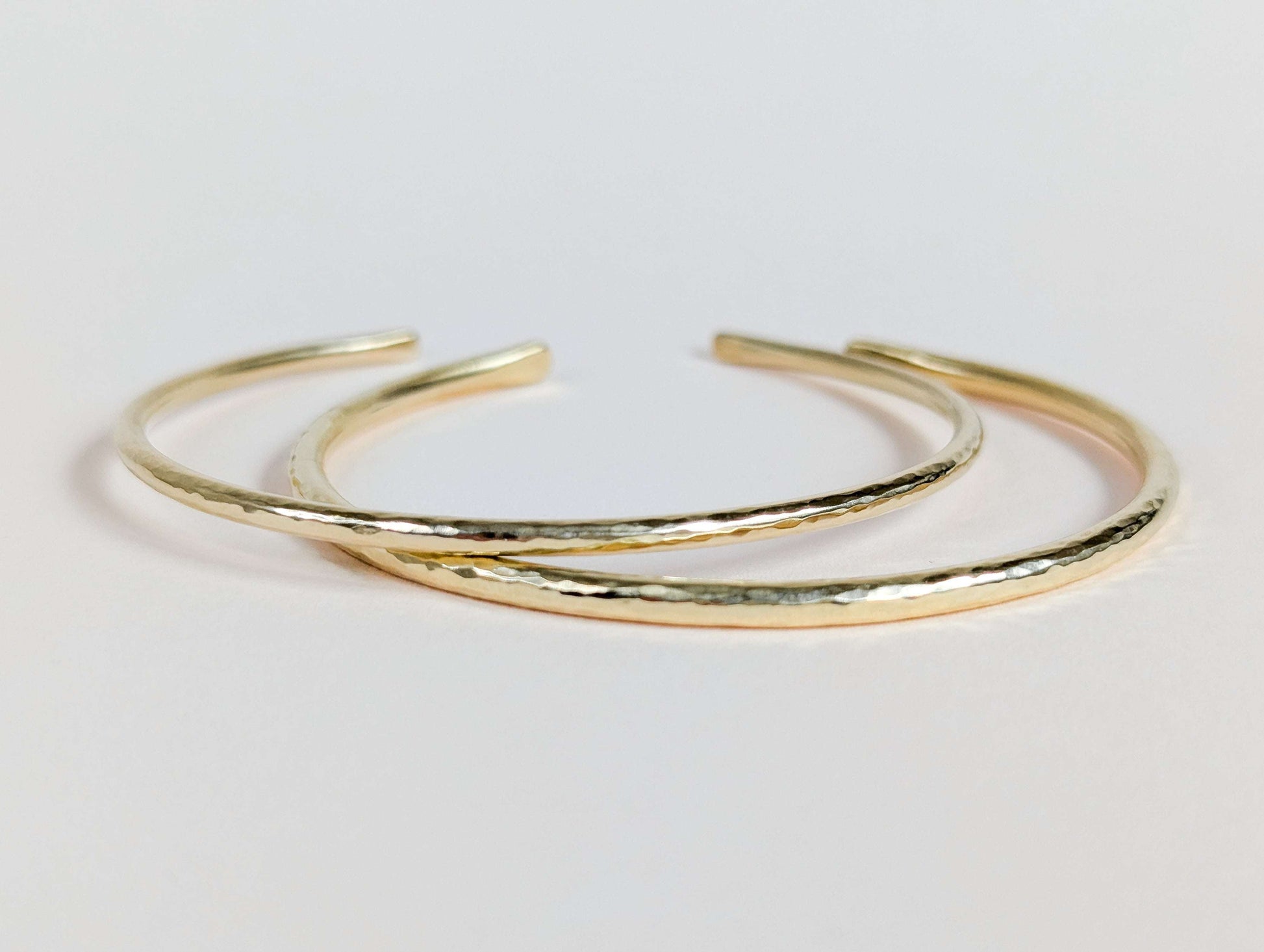 Two gold bangles on a light pink background