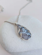 Dendritic snow agate leaf Necklace with a pendant on a light grey surface