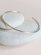 Silver bangle on a light stone surface with a soft pink background