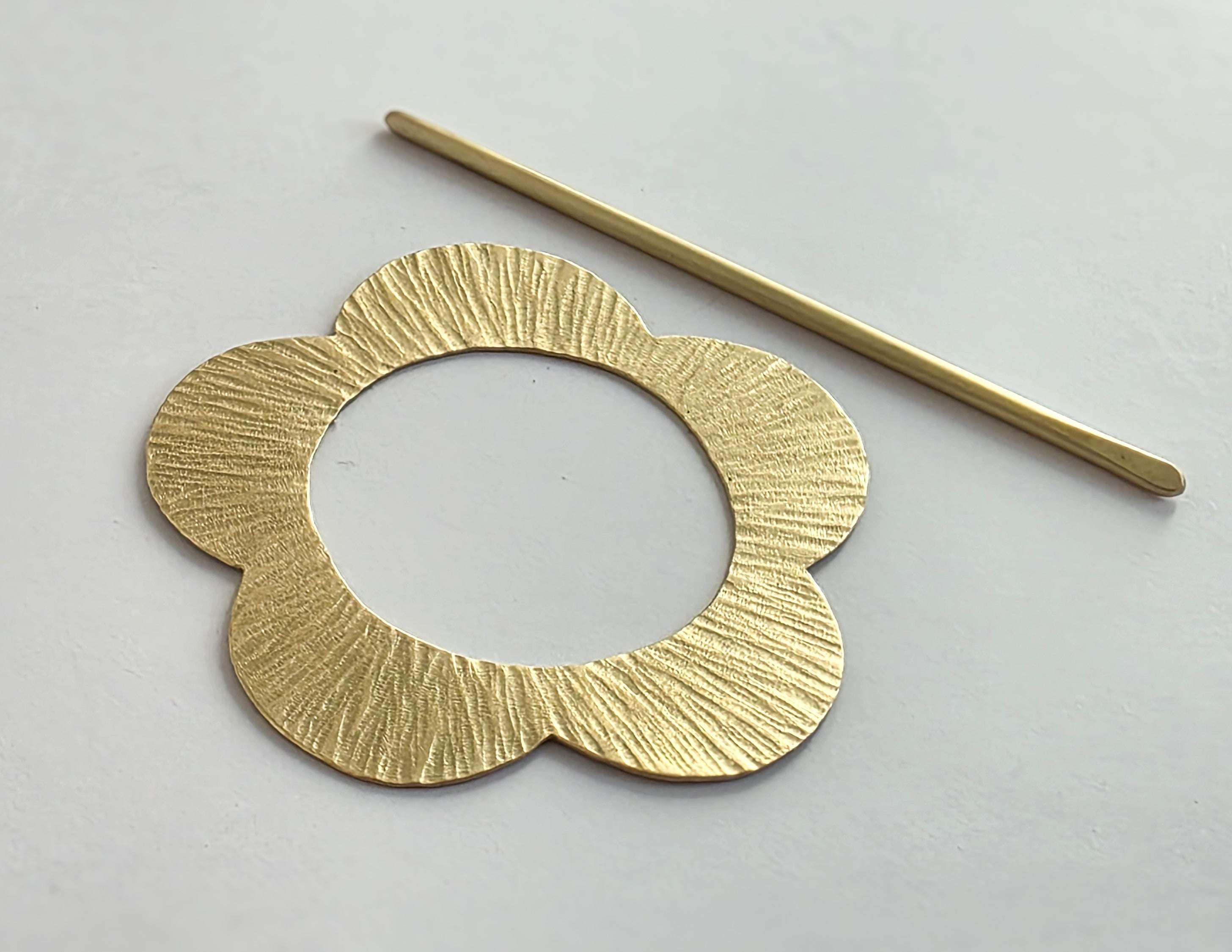 Gold circular earring and pin on a light gray background