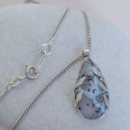 Dendritic snow agate leaf Necklace with a pendant on a light grey surface