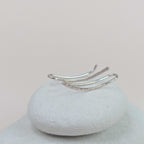 Silver ear climbers on a textured white surface with a light pink background