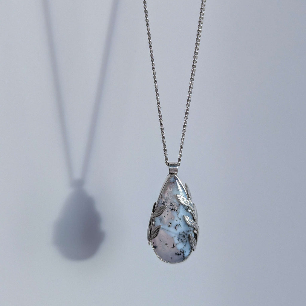 Dendritic snow agate leaf Necklace with a teardrop-shaped pendant on a light grey surface on a chain against a light grey background