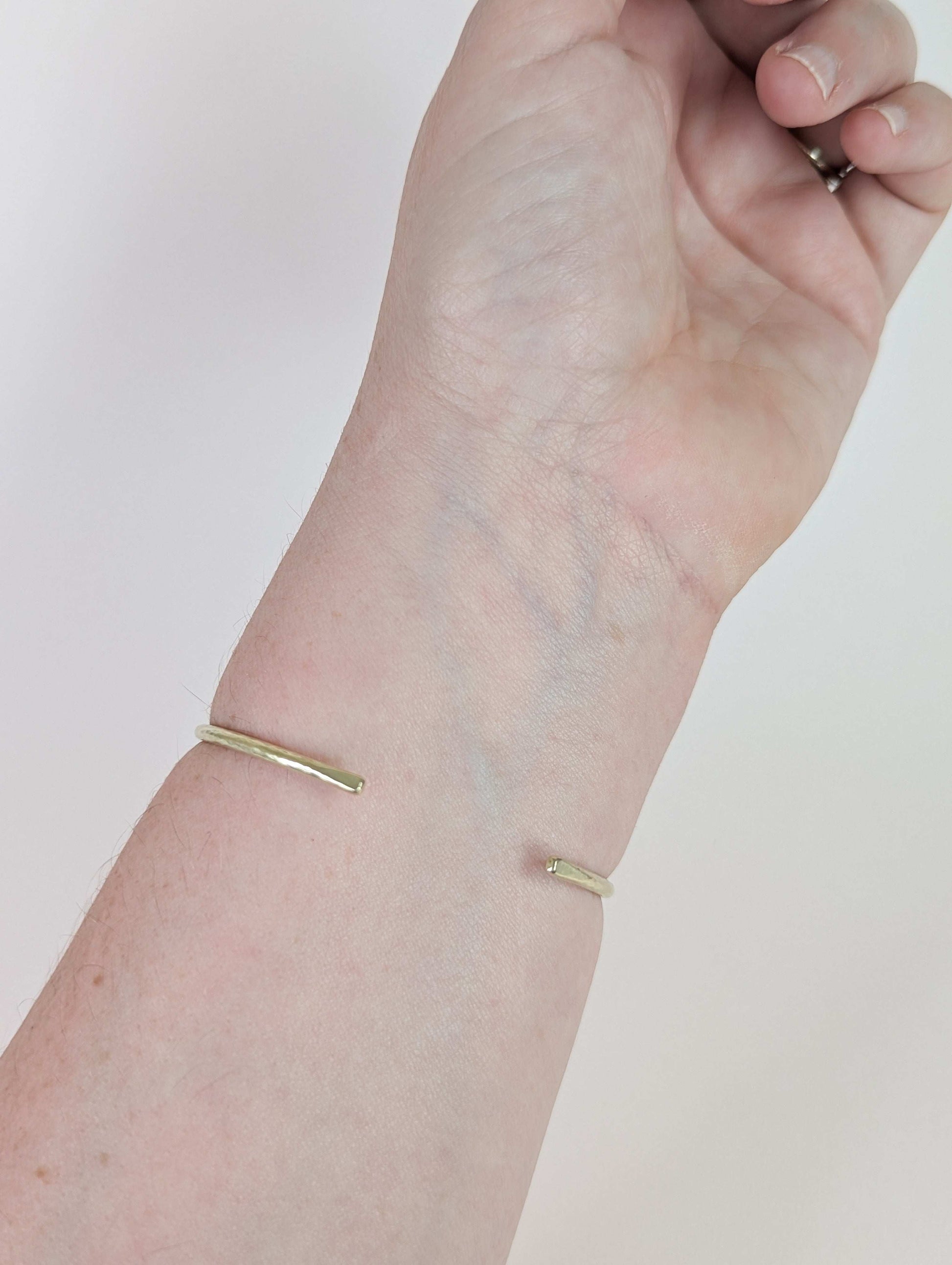 Gold bracelet on a wrist against a plain background