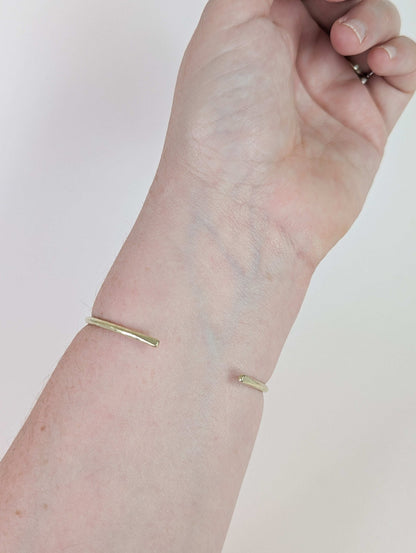 Gold bracelet on a wrist against a plain background