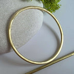 Gold brass hair barrette on a light grey surface with a textured stone and greenery in the background