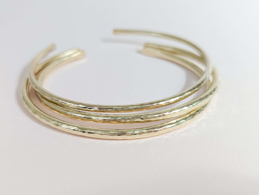 Three gold bangles stacked on a light pink background