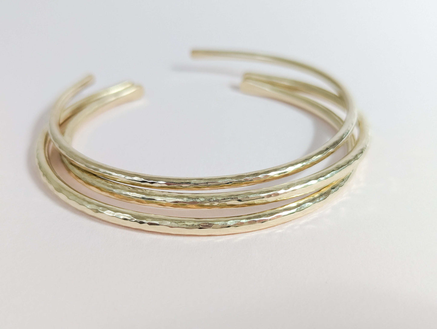 Three gold bangles stacked on a light pink background