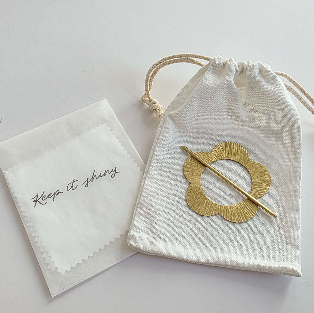 Gold brooch in a drawstring bag with a cloth labeled 'Keep it shining' on a light background