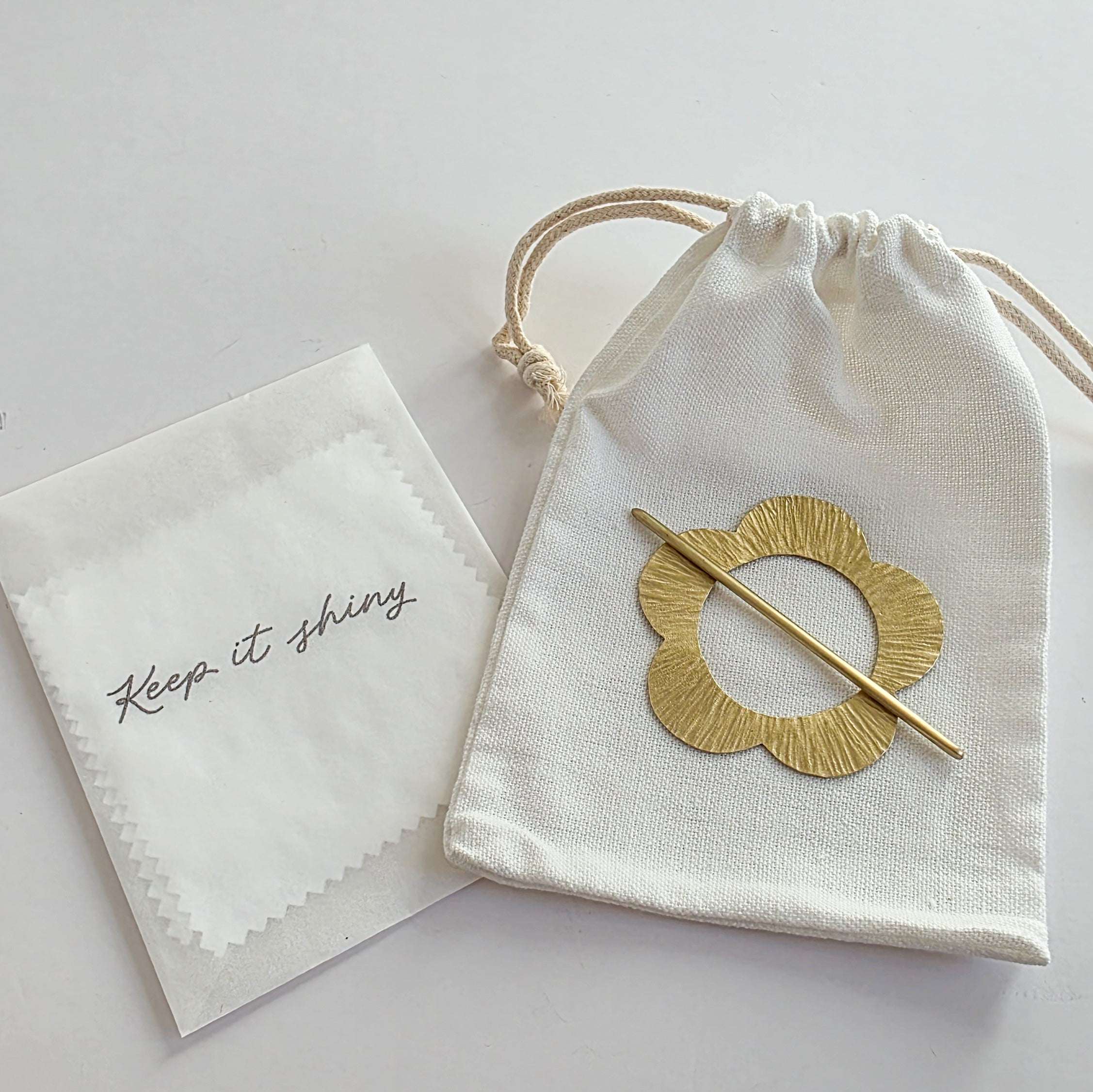 Gold brooch in a drawstring bag with a cloth labeled 'Keep it shining' on a light background